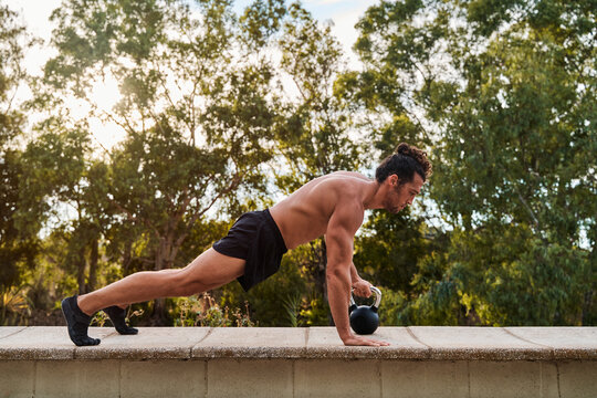 Athletic man performing kettlebell push ups outdoors in a park