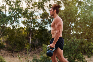 Muscular sportsman carrying kettlebell while exercising outdoors