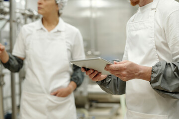 Workers inspecting food processing equipment in modern factory setting, wearing hygienic protective clothing, holding tablet device for monitoring and recording data