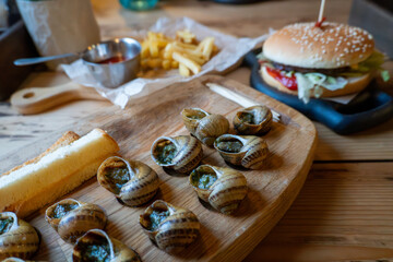 Delicious escargot and cheeseburger with fries on wooden table
