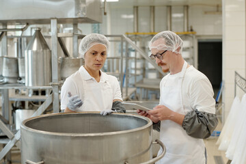 Two professionals in a commercial kitchen are using digital tablet while conducting a food safety inspection in well-equipped food processing facility