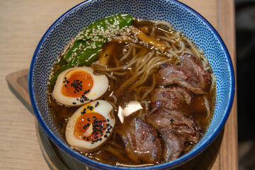 Savory bowl of ramen features tender noodles, soft boiled eggs with bright orange yolks, and fresh green peppers. Enjoyed in a warm, welcoming dining environment.
