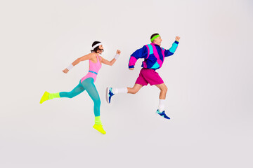 Energetic young couple jumping mid-air in colorful retro workout outfits on a clean white background, showcasing a fun and dynamic fitness