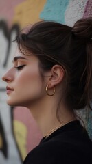 Fototapeta premium Serene Young Woman with Gold Hoops Posing Against a Graffiti Wall Urban Portrait Photography