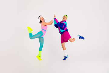 Energetic couple striking a retro aerobics pose with vibrant sportswear on a white background