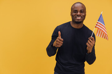Young african american man holding United States flag and showing thumbs up on yellow background