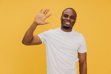 Smiling Young Man Waving Hand on Yellow Background