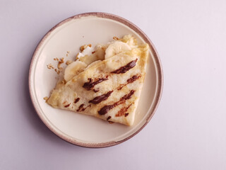 crepe with banana and chocolate on isolated brown plate and  light background
