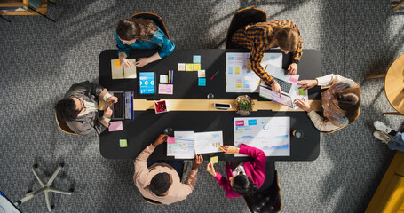 Top Down View: Diverse and Creative Colleagues Working Together at The Conference Table In Stylish Office. Male and Female Business People Using Tablets, and Laptops to Analyze Business Data on Charts