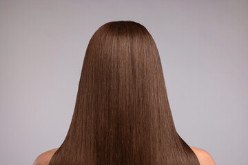 Woman with beautiful hair in mocha mousse shade on grey background, back view. Trendy color of 2025...