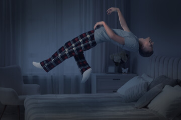 Sleepwalking. Young man floating over bed at home, toned in blue