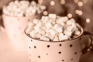 Delicious cocoa drink with marshmallows on table against blurred lights, toned in mocha mousse shade. Trendy color of 2025 year