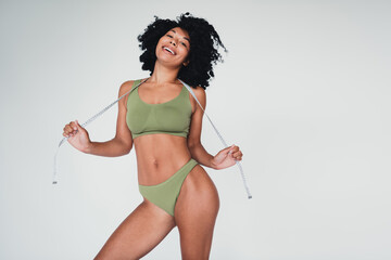 Confident young woman in stylish activewear holding measuring tape against a white background