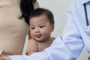 Pediatric doctor engaging with playful baby during a routine checkup with mother