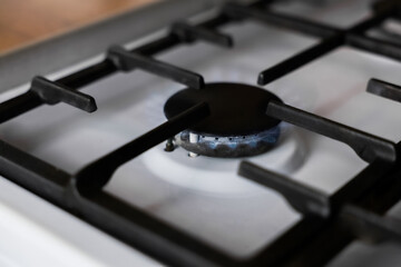 Close-up of a white gas stove with a black cast-iron grate and a black burner on which a blue fire...