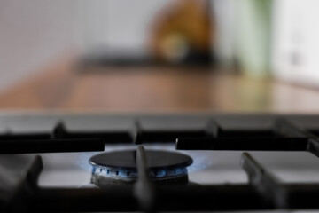 Close-up of a white gas stove with a black cast-iron grate and a black burner on which a blue fire burns against the background of a wooden kitchen in out-of-focus. Gas stove, cooking concept. High