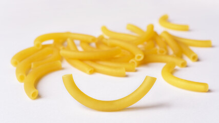 Dry tube shaped curved macaroni on white background. Close up photograph with selective focus on one single pasta.