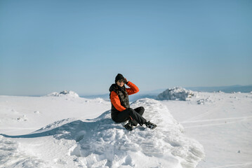 Woman sitting on a stone in the winter snowy mountain 