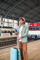 vertical latin Tourist holding smartphone and suitcase is waiting for train at station