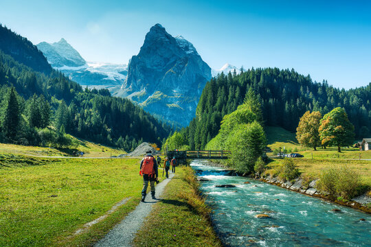 Tourists walking along the river with Rosenlaui mountain peak in lush forest at Bernese Alps, Switzerland
