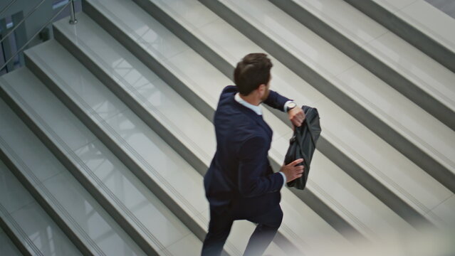 Hurrying businessman carrying briefcase climbing stairs inside office interior.