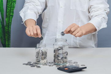 Businesswoman distributing coins into two glass jars. Concept of financial investment management, diversifying portfolio to reduce risks.