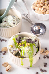 Dubai Chocolate Ice Cream, bowl with pistachio ice cream with tahini, kataifi and chocolate drops, with Dubai chocolate flavored syrup topping and pistachio nuts, on white kitchen table, copy space