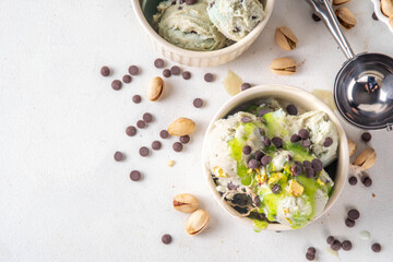 Dubai Chocolate Ice Cream, bowl with pistachio ice cream with tahini, kataifi and chocolate drops, with Dubai chocolate flavored syrup topping and pistachio nuts, on white kitchen table, copy space