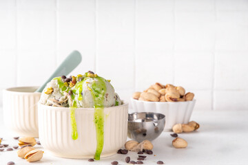Dubai Chocolate Ice Cream, bowl with pistachio ice cream with tahini, kataifi and chocolate drops, with Dubai chocolate flavored syrup topping and pistachio nuts, on white kitchen table, copy space
