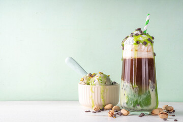 Dubai Chocolate Ice Cream iced coffee latte with pistachio ice cream, tahini, kataifi, whipped cream chocolate drops and dubai chocolate flavored syrup, on white green table, copy space