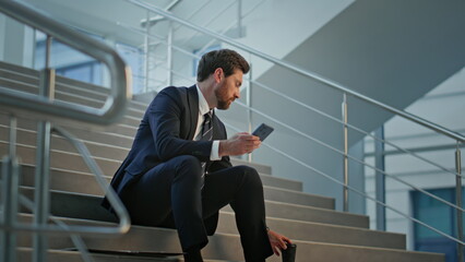 Professional entrepreneur sitting stairs office checking phone holding coffee.