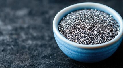 Vitamin and metabolism essential, A close-up of a blue bowl filled with tiny black seeds, set against a dark surface, showcasing the texture and color contrast.