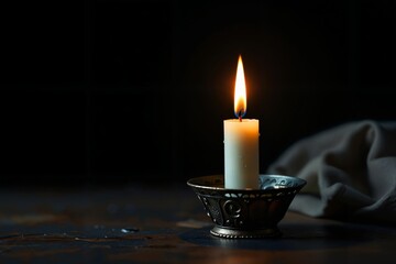 Eine brennende Kerze in einem metallenen Kerzenhalter steht im Fokus vor dunklem Hintergrund und das weiche Licht betonen die flackernde Flamme, die Hoffnung und Erinnerung symbolisiert.