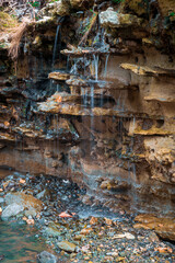 A tranquil waterfall gently flowing over rugged, layered rock formations. The interplay of water and stone creates a soothing atmosphere, enhanced by the lush greenery surrounding the scene