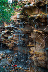 Fototapeta premium A tranquil waterfall gently flowing over rugged, layered rock formations. The interplay of water and stone creates a soothing atmosphere, enhanced by the lush greenery surrounding the scene