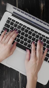 Close-up view of a woman hands typing on a laptop computer keyboard at an office. Modern work and professional activity in a business setting. Vertical video.