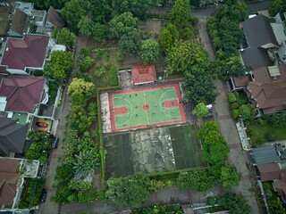 Obraz premium Drone shot of a basketball court nestled in a suburban neighborhood. Lush greenery surrounds the court.
