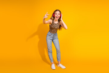 Trendy young woman in leopard print top enjoys music against vibrant yellow background