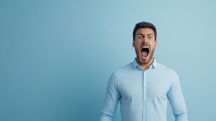 Obraz premium Man in Light Blue Shirt Expressing Intense Emotion with Open Mouth Against a Solid Light Blue Background