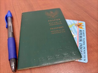 An Indonesian passport, identity card (KTP), and blue pen on a wooden table. Represents travel, identity verification, legal documents, and official paperwork. Ideal for travel or administrative theme