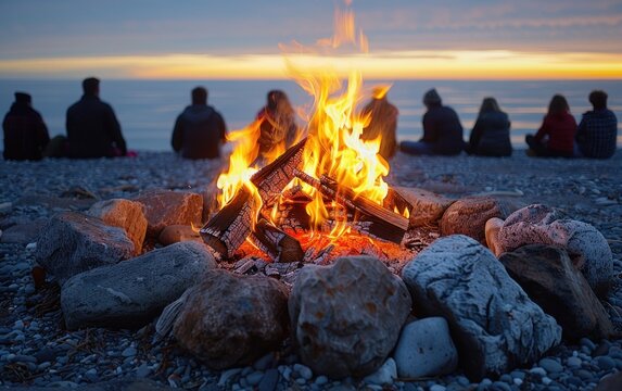 Friends gathered around a bonfire on a beach at sunset, enjoying the warmth and ambiance of the fire as the sun dips below the horizon. The scene is peaceful and evokes a sense of community and relaxa