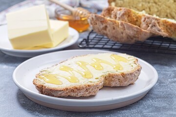 Freshly baked white Irish soda bread with butter and honey served on a plate, horizontal