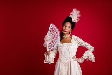 Captivating portrayal of a young woman in vintage attire with a fan against a bold red background