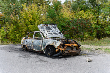 Burned car wreck abandoned on roadside in nature