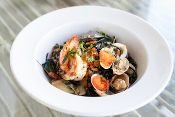 Squid ink spaghetti with garlic, olive oil, chili and seafood on white dish.