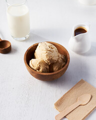 A bowl filled with creamy ice cream sits beside a glass of milk and a small pitcher of syrup on a simple white table, inviting indulgence