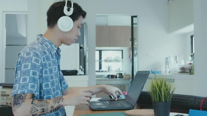 A young individual is engaged in work while wearing headphones, using a laptop. The image captures a relaxed workspace environment, featuring minimalistic decor and a plant in the background, promotin