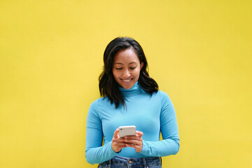 Young woman smiling and using mobile phone against yellow background