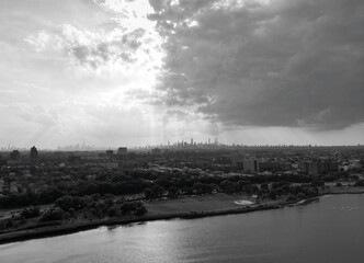 Fototapeta premium aerial view of new york city skyline from corona flushing meadows park with dramatic dark sky coming clouds at sunset (lake distant skyscrapers of manhattan far away) horizon silhouette shadow queens