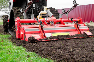 Obraz premium Plowing and milling the land on a garden plot. A crawler tractor with a milling cutter plows the land